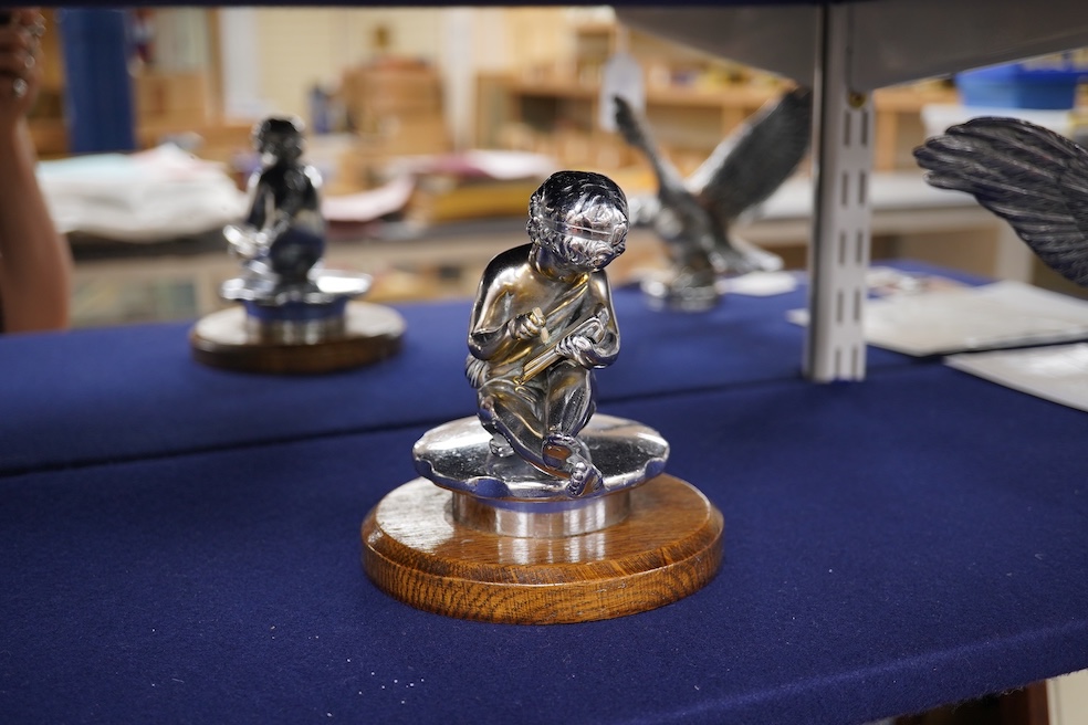 Two chrome car mascots, one in the form of an eagle stamped Finnigans London, wingspan 26cm, and the other of a classical child writing, mounted on a substantial radiator cap and oak base. Condition - fair to good, some